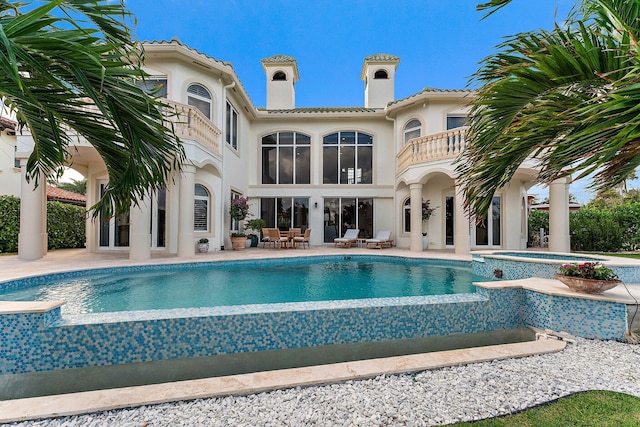 back of house featuring a swimming pool with hot tub, a patio, and a balcony