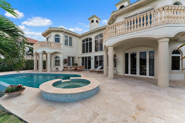 rear view of house featuring a swimming pool with hot tub, a balcony, a patio, and french doors