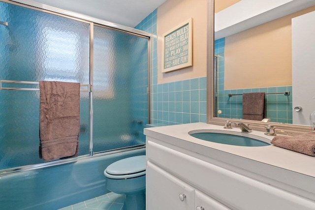 full bathroom featuring combined bath / shower with glass door, tile patterned floors, vanity, tile walls, and toilet