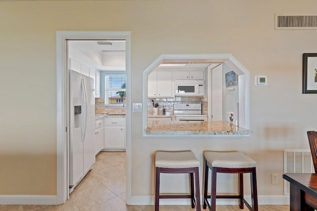 kitchen featuring light stone countertops, backsplash, white appliances, a breakfast bar, and white cabinets