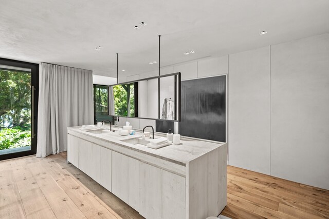 kitchen with decorative light fixtures, light wood-type flooring, a center island with sink, and white cabinetry