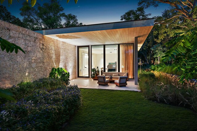 back house at dusk featuring a yard, an outdoor hangout area, and a patio area