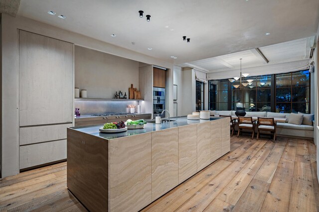 kitchen with sink, stainless steel gas cooktop, light hardwood / wood-style flooring, an island with sink, and a chandelier