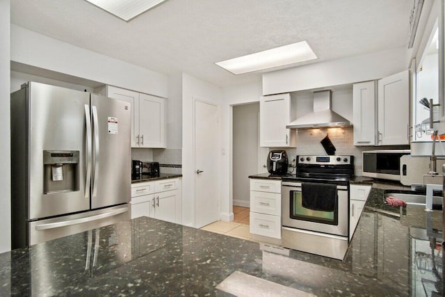 kitchen featuring white cabinets, decorative backsplash, stainless steel appliances, and wall chimney exhaust hood