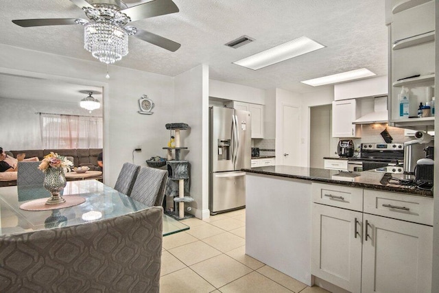 kitchen with dark stone counters, wall chimney range hood, a textured ceiling, appliances with stainless steel finishes, and light tile patterned flooring