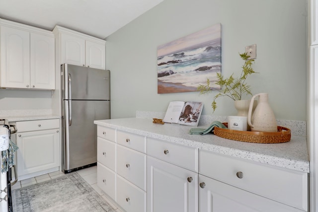 kitchen with white cabinets, stainless steel fridge, light stone counters, and light tile patterned flooring