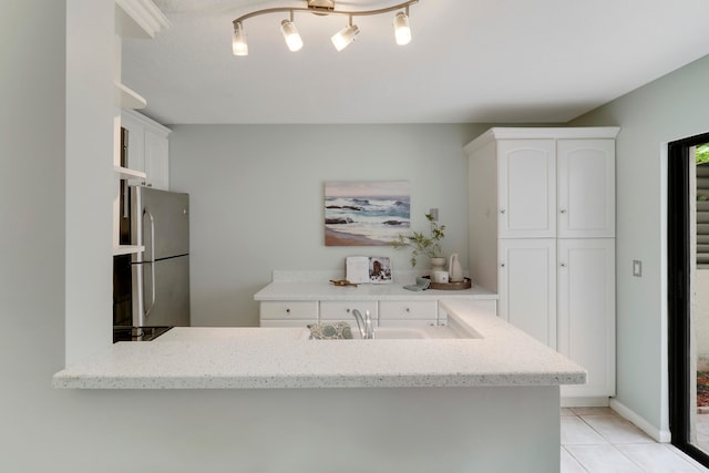 kitchen with light tile patterned flooring, light stone countertops, white cabinetry, and stainless steel refrigerator