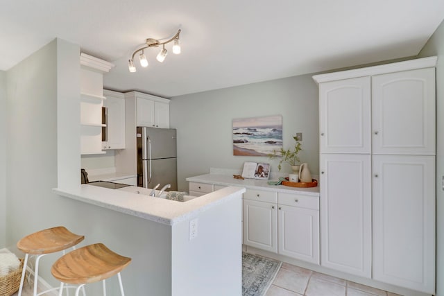 kitchen featuring a kitchen bar, stainless steel fridge, kitchen peninsula, black range, and white cabinets