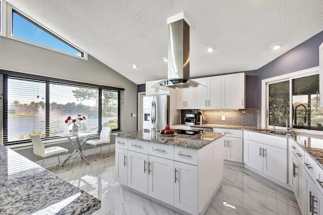 kitchen featuring island exhaust hood, light stone counters, double oven, white cabinets, and a kitchen island