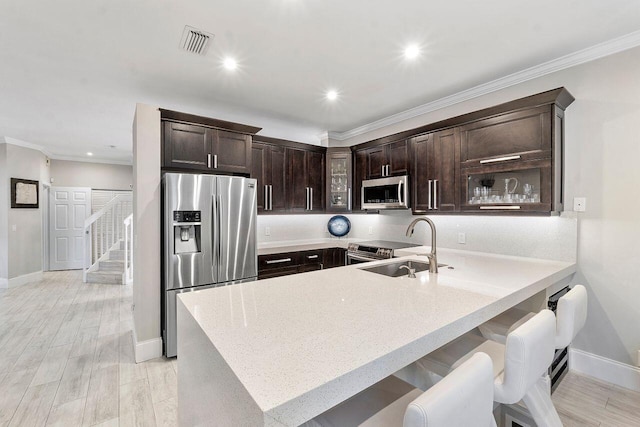 kitchen with kitchen peninsula, appliances with stainless steel finishes, a kitchen bar, dark brown cabinets, and light hardwood / wood-style floors