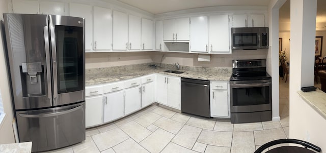 kitchen featuring sink, light tile patterned floors, appliances with stainless steel finishes, light stone countertops, and white cabinets