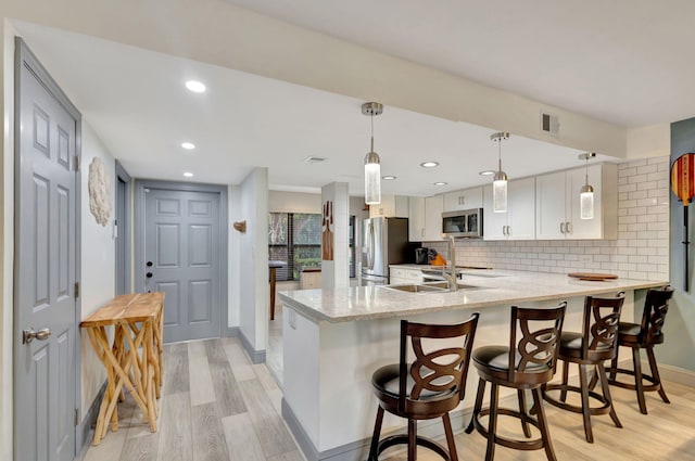 kitchen featuring white cabinets, light wood-type flooring, tasteful backsplash, kitchen peninsula, and stainless steel appliances