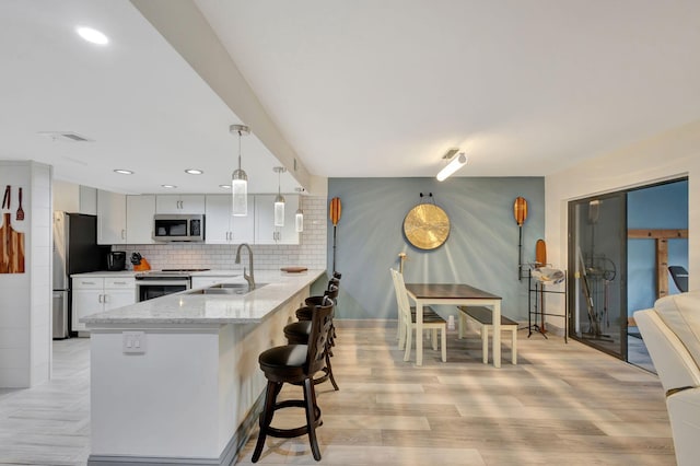 kitchen featuring decorative light fixtures, light hardwood / wood-style floors, kitchen peninsula, and appliances with stainless steel finishes