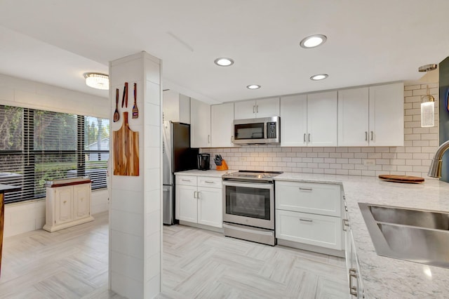 kitchen featuring backsplash, light stone counters, stainless steel appliances, sink, and white cabinetry