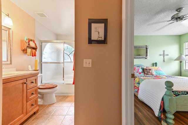 full bathroom with vanity, tile patterned floors, bath / shower combo with glass door, toilet, and a textured ceiling