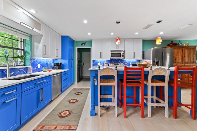 kitchen featuring stainless steel appliances, sink, decorative light fixtures, a center island, and white cabinetry