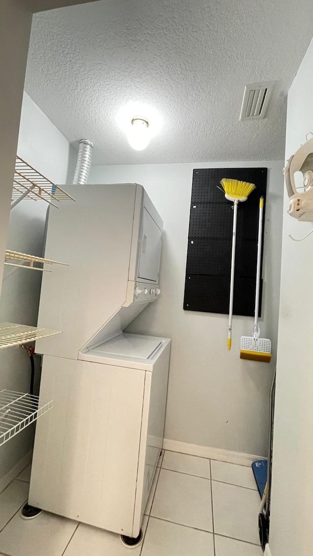 clothes washing area featuring light tile patterned floors, a textured ceiling, and stacked washer and clothes dryer