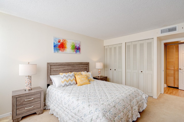 carpeted bedroom featuring a textured ceiling and two closets