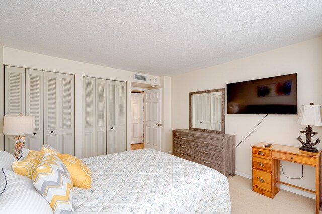 bedroom featuring multiple closets, light carpet, and a textured ceiling