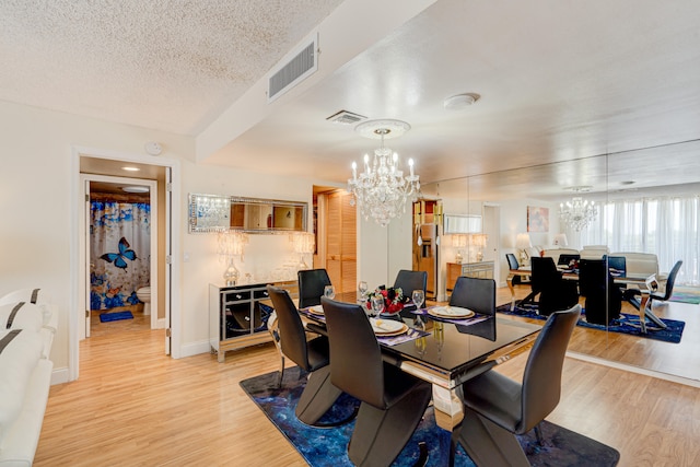 dining room with light hardwood / wood-style floors, a textured ceiling, and an inviting chandelier