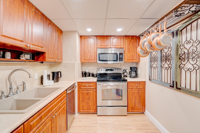 kitchen with a drop ceiling, sink, light wood-type flooring, tasteful backsplash, and stainless steel appliances