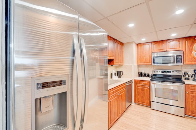 kitchen with a paneled ceiling, decorative backsplash, light hardwood / wood-style floors, and appliances with stainless steel finishes