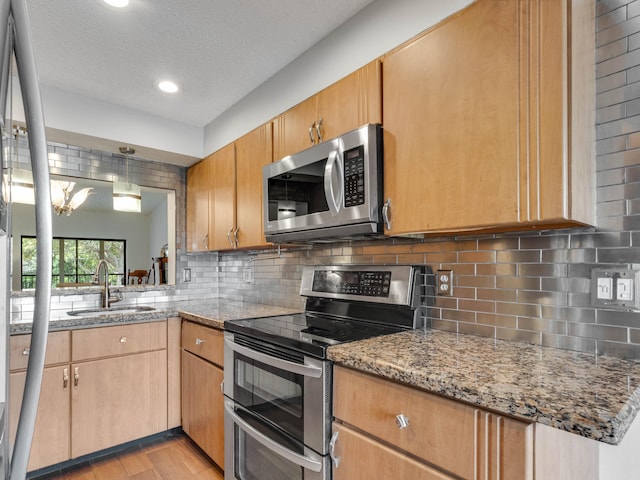 kitchen featuring light stone counters, light wood finished floors, decorative backsplash, appliances with stainless steel finishes, and a sink