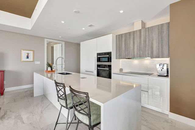 kitchen featuring sink, a kitchen bar, black electric cooktop, a kitchen island with sink, and white cabinets