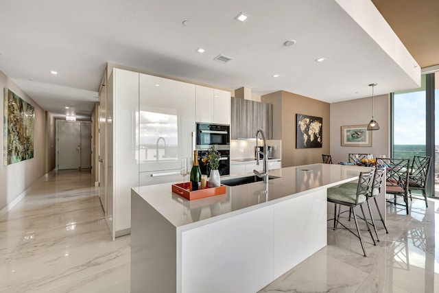 kitchen featuring white cabinets, black double oven, an island with sink, and pendant lighting