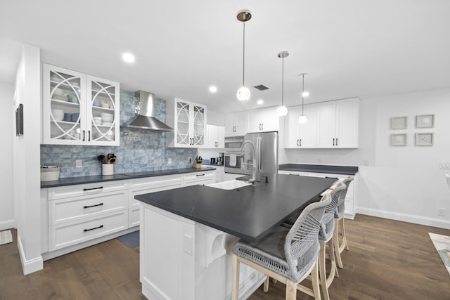 kitchen with a center island with sink, wall chimney exhaust hood, dark hardwood / wood-style floors, and white cabinets