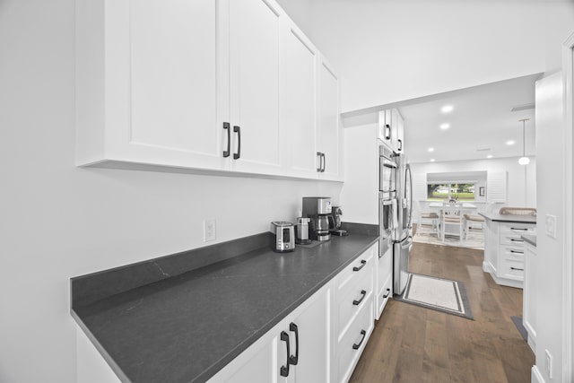 kitchen featuring white cabinetry, stainless steel appliances, dark hardwood / wood-style floors, dark stone countertops, and pendant lighting