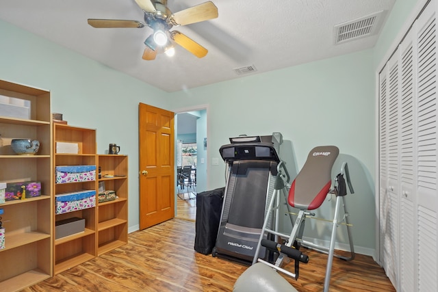 workout area with ceiling fan, light hardwood / wood-style floors, and a textured ceiling