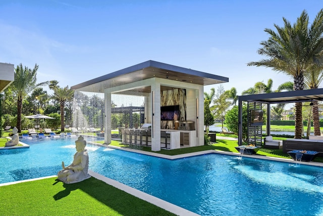 view of swimming pool with pool water feature, exterior kitchen, an outdoor bar, and a lawn