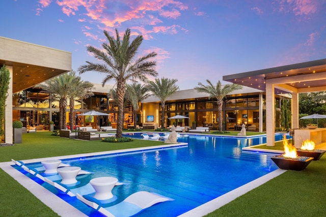 pool at dusk featuring a lawn, a patio area, an in ground hot tub, and a fire pit