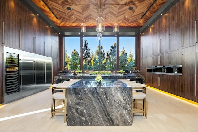 bar with hanging light fixtures, a high ceiling, dark stone countertops, built in refrigerator, and wood walls