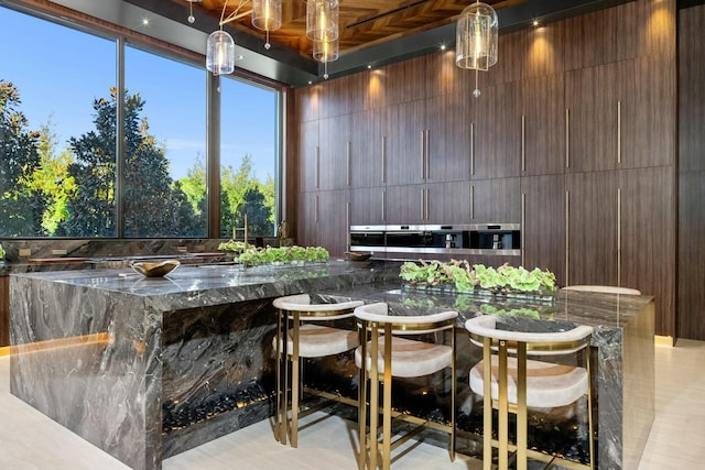 bar featuring dark stone counters, dark brown cabinets, light tile patterned floors, and hanging light fixtures