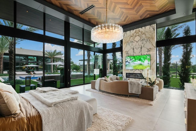 bedroom featuring a towering ceiling, an inviting chandelier, expansive windows, and a premium fireplace