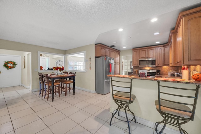 kitchen featuring decorative backsplash, a kitchen bar, dark stone counters, stainless steel appliances, and light tile patterned flooring