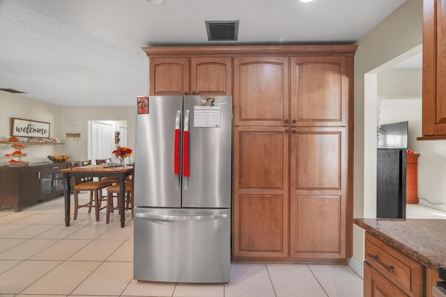 kitchen featuring stainless steel fridge, light tile patterned flooring, and a textured ceiling