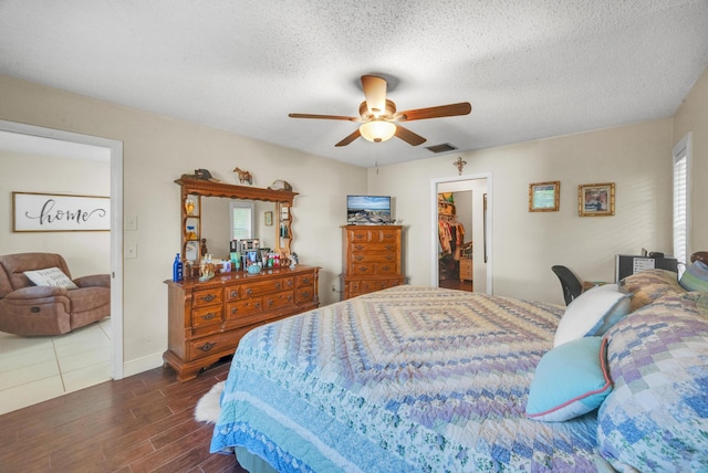 bedroom featuring dark hardwood / wood-style flooring, a textured ceiling, ceiling fan, a spacious closet, and a closet