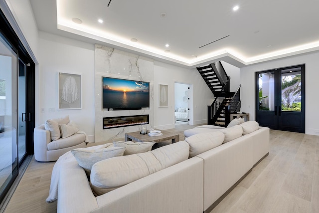 living room with a raised ceiling, a high end fireplace, and light wood-type flooring