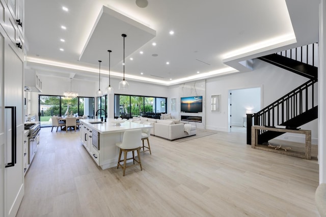 interior space with pendant lighting, a center island with sink, sink, a kitchen bar, and white cabinetry