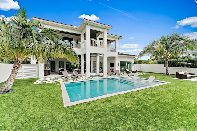 rear view of house featuring a patio, a balcony, a fenced in pool, and a lawn