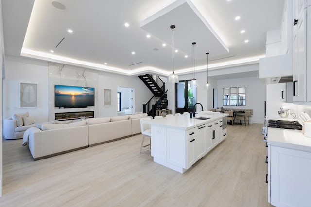 kitchen featuring a raised ceiling, sink, decorative light fixtures, a center island with sink, and white cabinetry