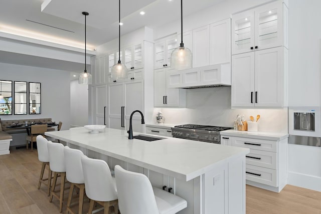 kitchen featuring white cabinets, sink, an island with sink, light hardwood / wood-style floors, and stainless steel range oven