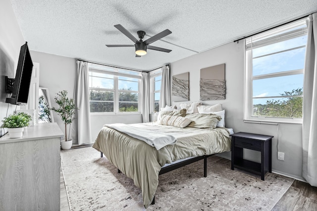 bedroom featuring multiple windows, ceiling fan, light hardwood / wood-style flooring, and a textured ceiling