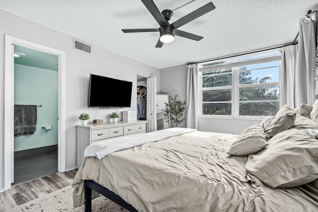 bedroom with ensuite bath, ceiling fan, a spacious closet, a textured ceiling, and light wood-type flooring