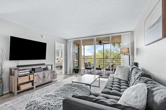 living room featuring ceiling fan, light hardwood / wood-style floors, a wall of windows, and a textured ceiling