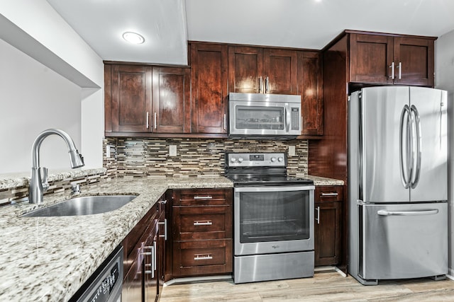 kitchen with appliances with stainless steel finishes, light wood-type flooring, backsplash, light stone counters, and sink