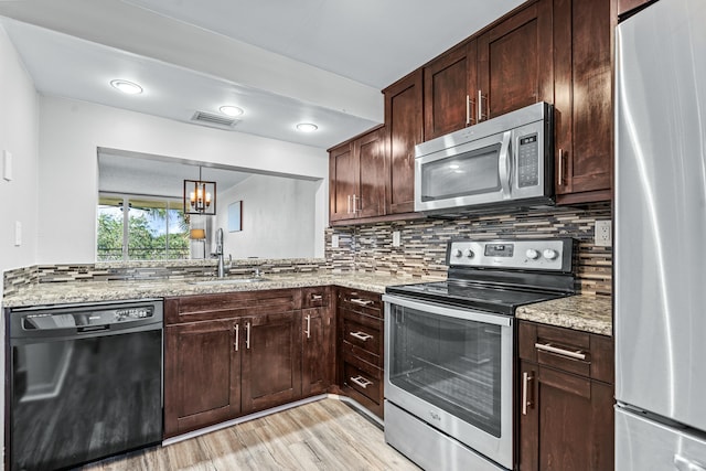 kitchen featuring sink, light wood-type flooring, appliances with stainless steel finishes, light stone counters, and a chandelier